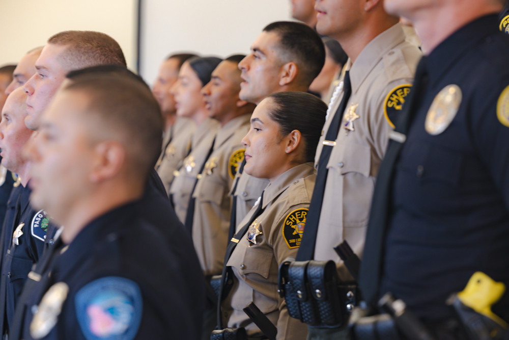 Law enforcement recruits stand in uniform during Allan Hancock College’s Law Enforcement Academy graduation ceremony in Lompoc on December 3, 2025. The group, consisting of 26 graduates, includes recruits from various local agencies wearing tan sheriff and dark police uniforms, facing forward in formation.